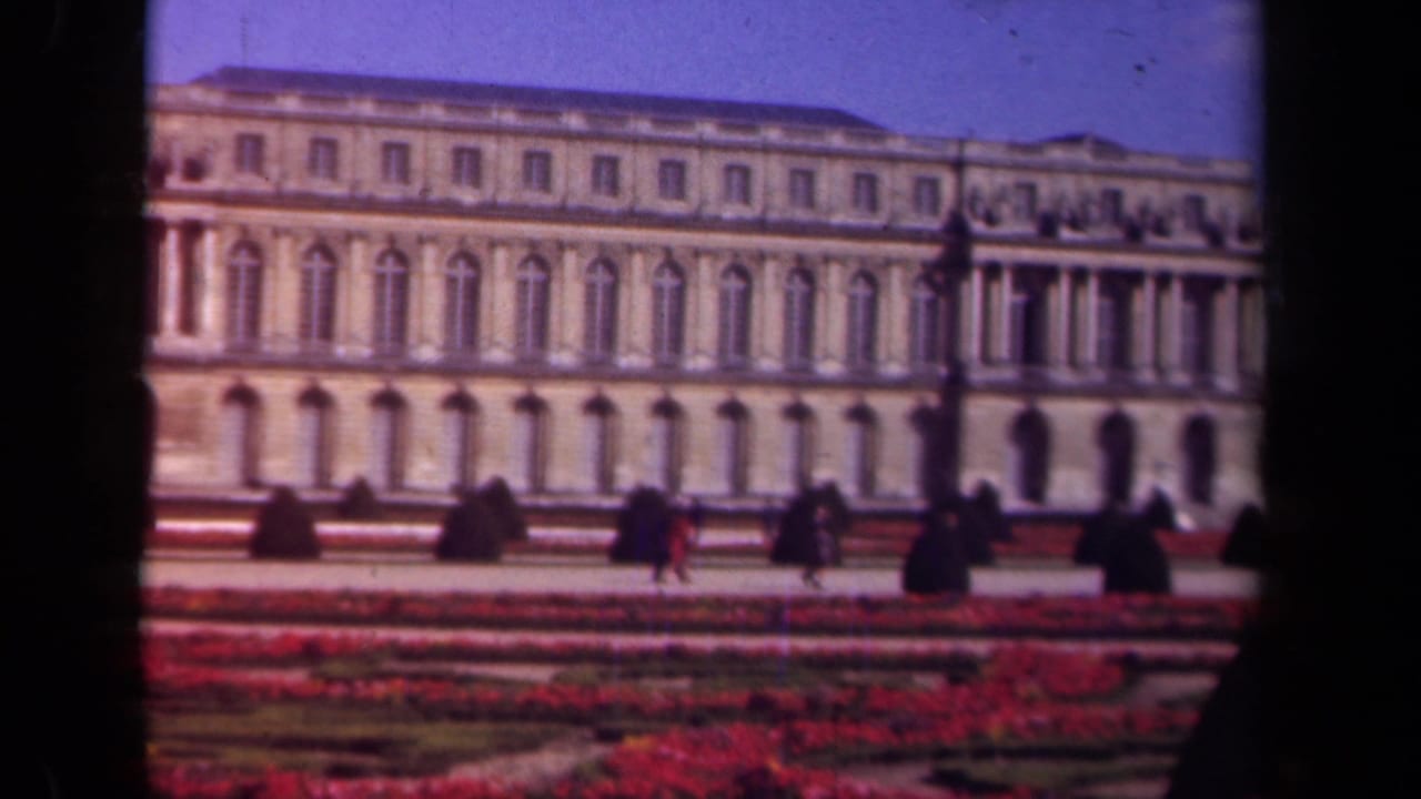 1939 Paris home-movie frame of a monumental historic building, red garden beds, topiary shrubs, and visitors on the grounds.