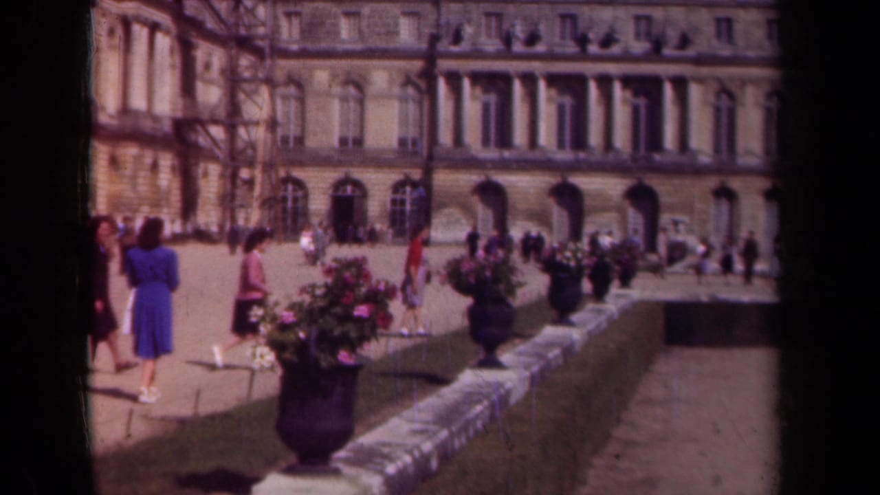 1939 Paris visitor footage showing people in period dress near flower planters and a stone facade with arched colonnades.