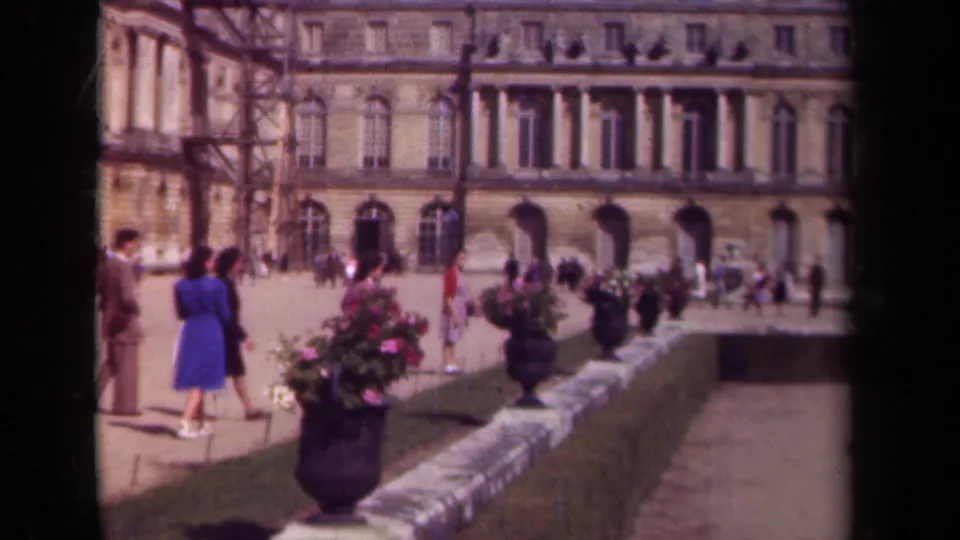 1939 Paris 8mm frame showing visitors near a flower planter, stone railing, and arched facade of a historic public building.