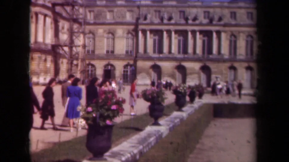 Paris, 1939 home-movie view of people pausing near potted flowers on palace grounds, with columns, arched windows, and scaffolding visible.