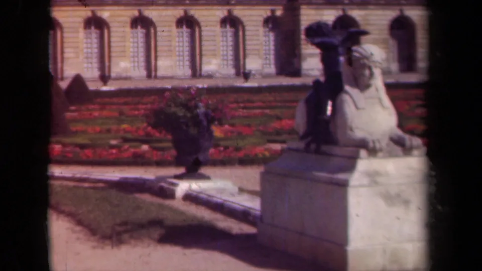 1939 Paris frame showing the sphinx statue from a similar angle with formal planting and a stone landmark facade behind it.