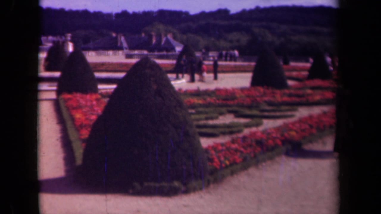 Formal Paris garden in 1939 with red parterres, cone-shaped topiary, gravel paths, distant visitors, trees, and blue sky.