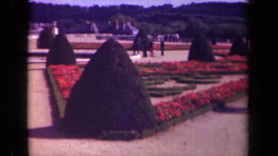 1939 Paris public garden view across red flower beds, clipped topiary, pale paths, distant visitors, and wooded background.