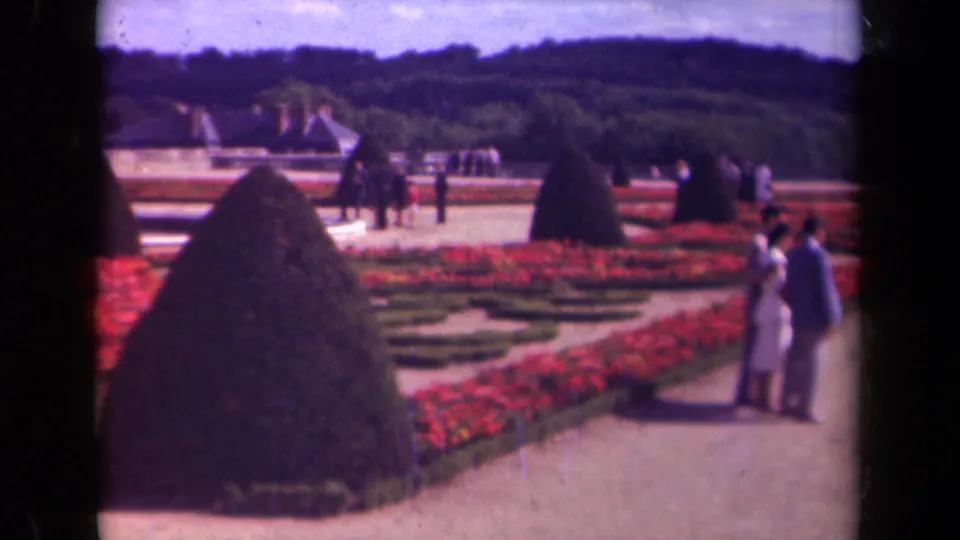1939 Paris garden scene with cone topiary, red parterres, gravel walks, wooded backdrop, and two visible visitors at right.