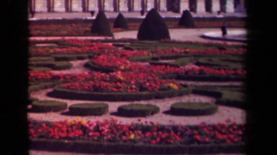 1939 Paris formal garden detail with circular hedge forms, red flower beds, cone topiary, gravel paths, and partial architecture.