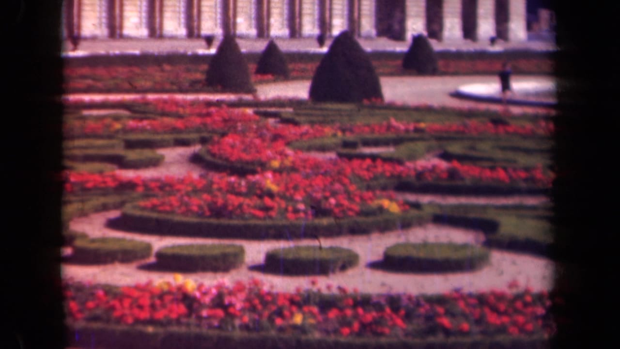 Paris-area 1939 garden footage showing red and pink planting beds, low clipped hedges, pale paths, topiary shapes, and a columned facade.