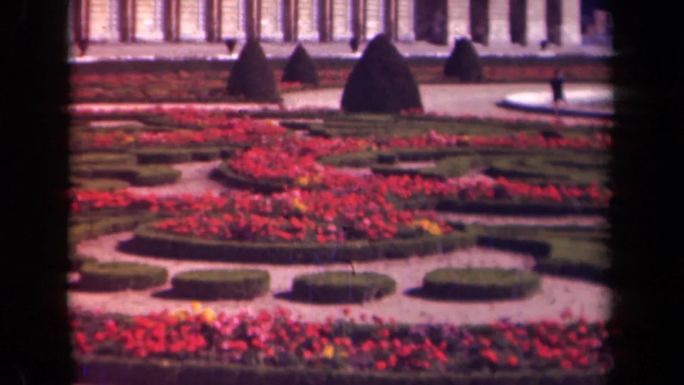 Paris-area 1939 garden footage showing red and pink planting beds, low clipped hedges, pale paths, topiary shapes, and a columned facade.