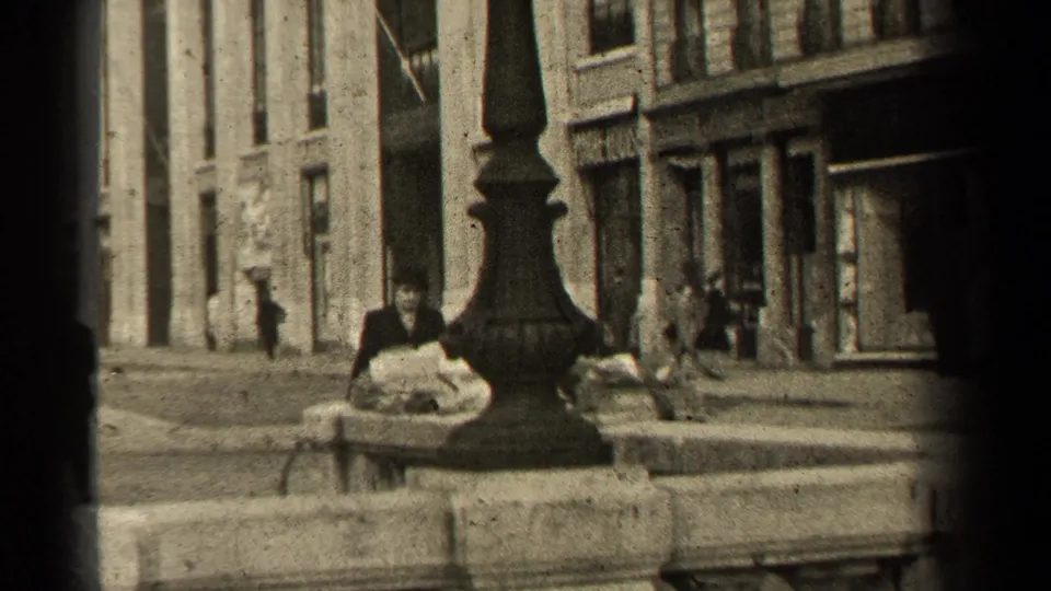 Paris sidewalk in 1947 with pedestrians near stone building fronts, a lamp base, curb railing, and soft 8mm vignetting.