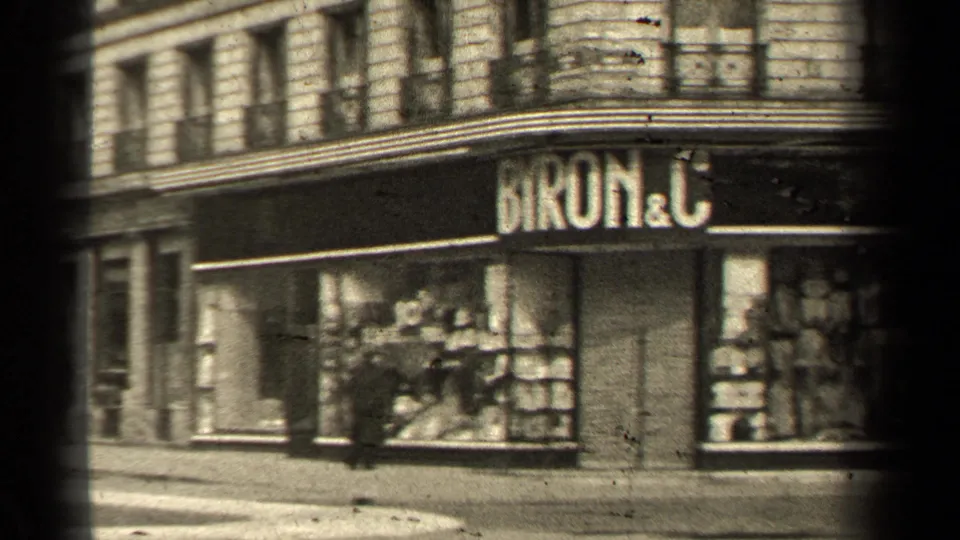 Angled 1947 Paris view of the BYRON & C corner storefront with display windows, sale signs, sidewalk, and balcony railings above.