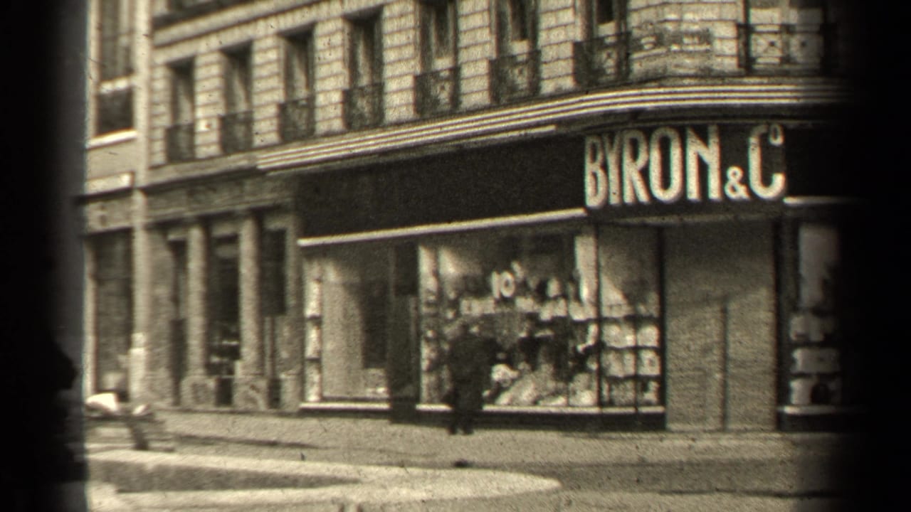 Paris street corner with Byron & C storefront, stone facade, shop windows, and a pedestrian near the curb.