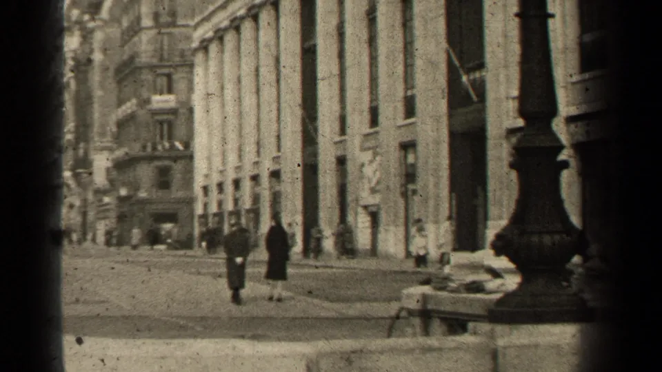 1947 Paris street perspective showing pedestrians walking between tall stone facades, shopfronts, and a foreground lamppost.