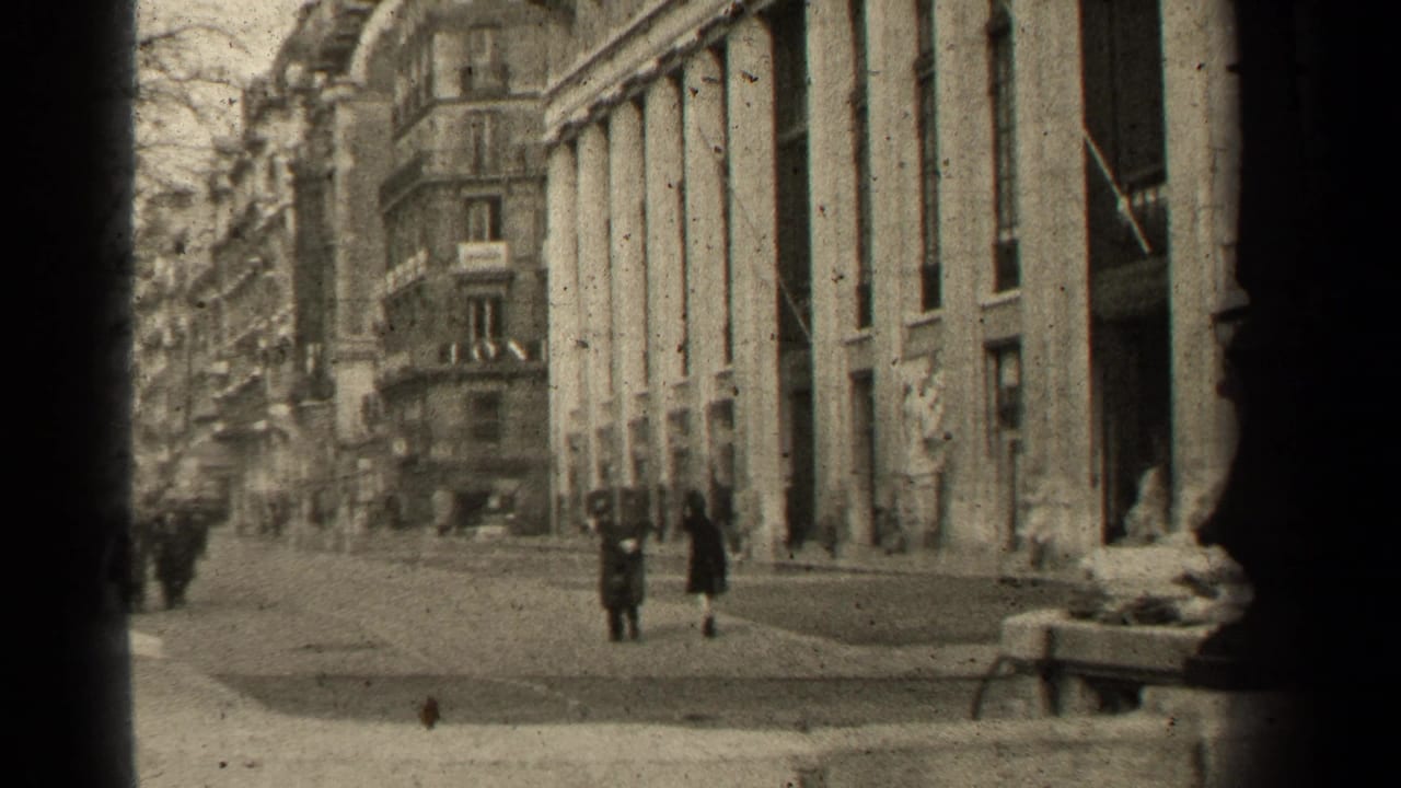 Pedestrians walk near tall columned buildings on a Paris street.