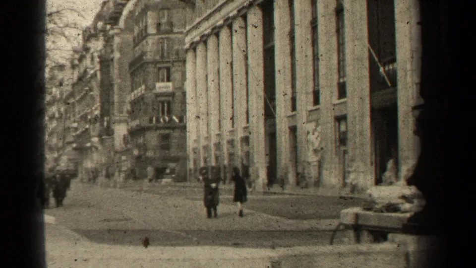 1947 Paris street view with pedestrians in coats passing a grand columned facade and apartment buildings.