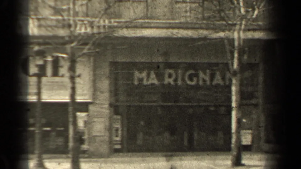 1947 Paris street frame showing Marignan-area storefront lettering, bare trees, sidewalk pedestrians, and dark 8mm gate edges.