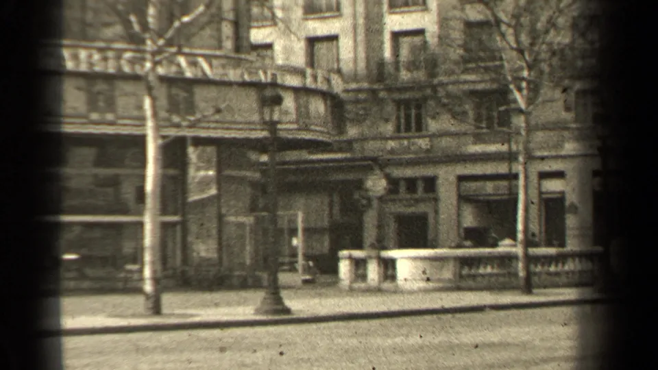 1947 Paris street corner showing shopfronts, upper-story windows, bare trees, lampposts, and a low stone railing.