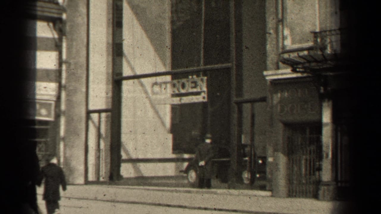 1947 Paris street view with pedestrians in coats moving past storefronts, a Citroen sign, masonry facades, and dark 8mm frame edges.