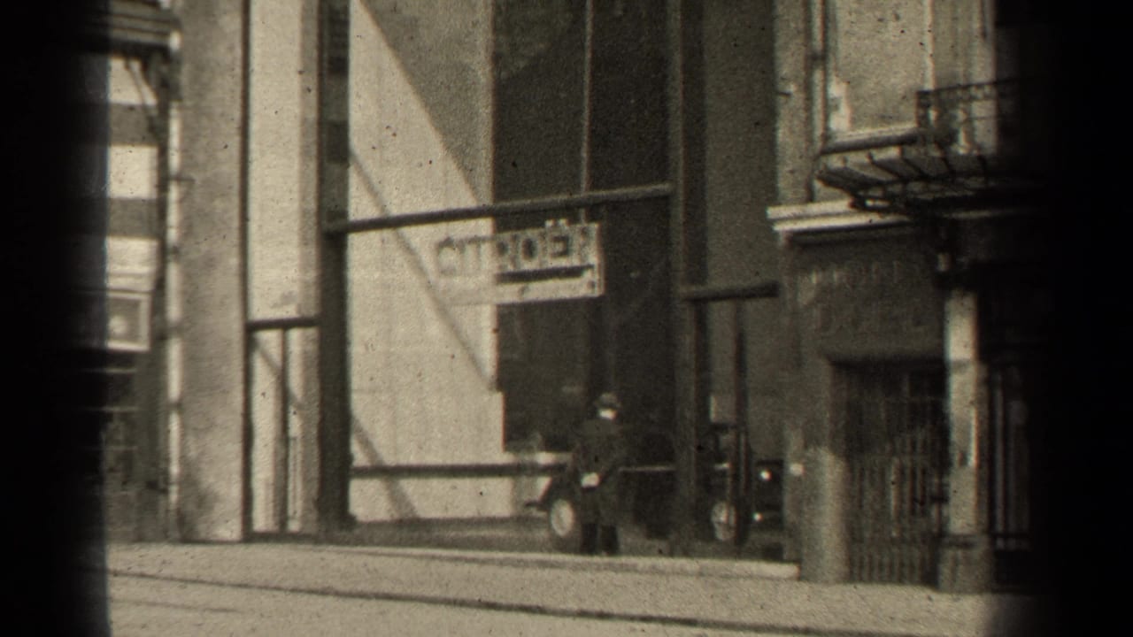 1947 Paris sidewalk scene with a pedestrian near a Citroen sign, storefront architecture, and visible gate-edge shadow from the 8mm scan.