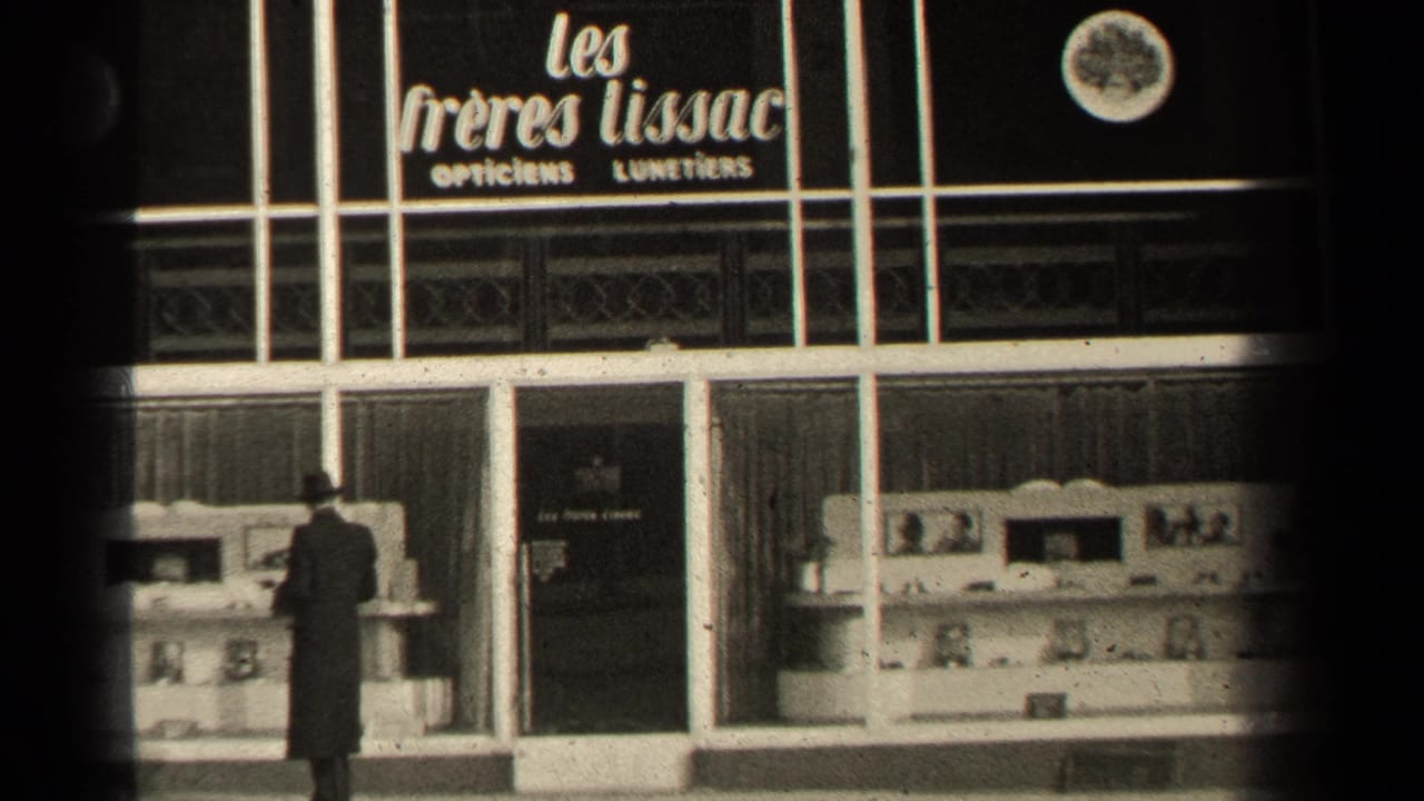 Man in a dark coat stands before a French optician storefront display.