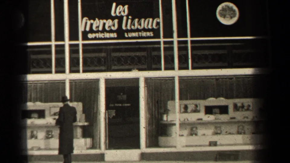 1947 Paris street view of a man in a dark overcoat facing the Les Freres Lissac optician window.