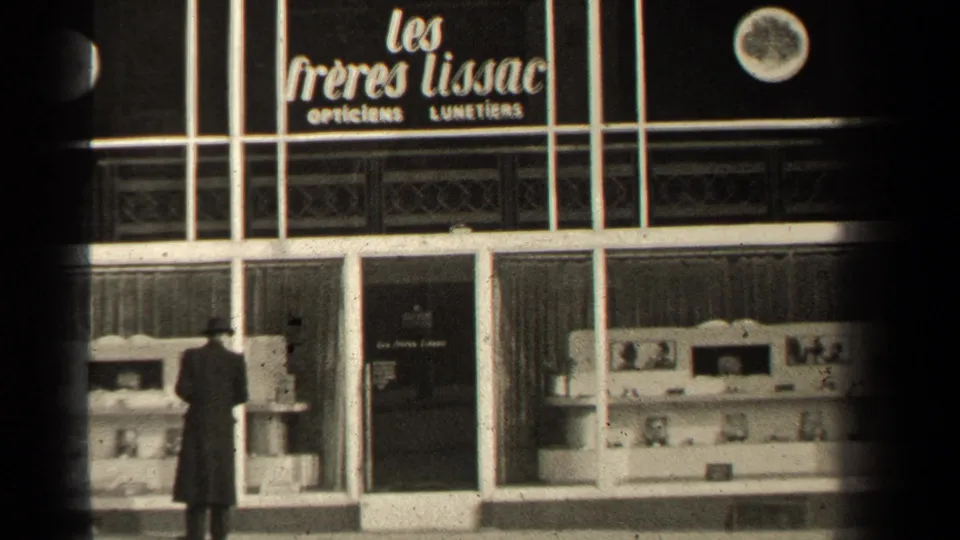 The man remains near the Paris optician display, with the shop name and glass-fronted facade visible.