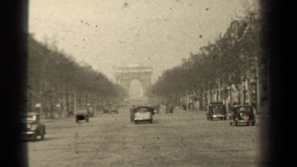 Wide view along the Champs-Elysees toward the Arc de Triomphe, with mid-century cars moving on the boulevard.