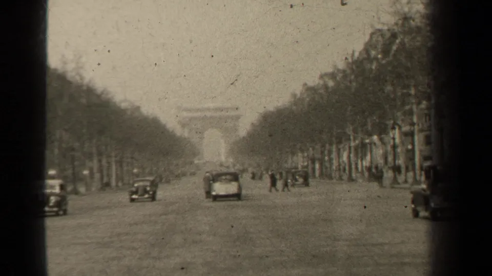 1947 Champs-Elysees footage with a car approaching, pedestrians crossing, trees lining both sides, and the Arc de Triomphe ahead.