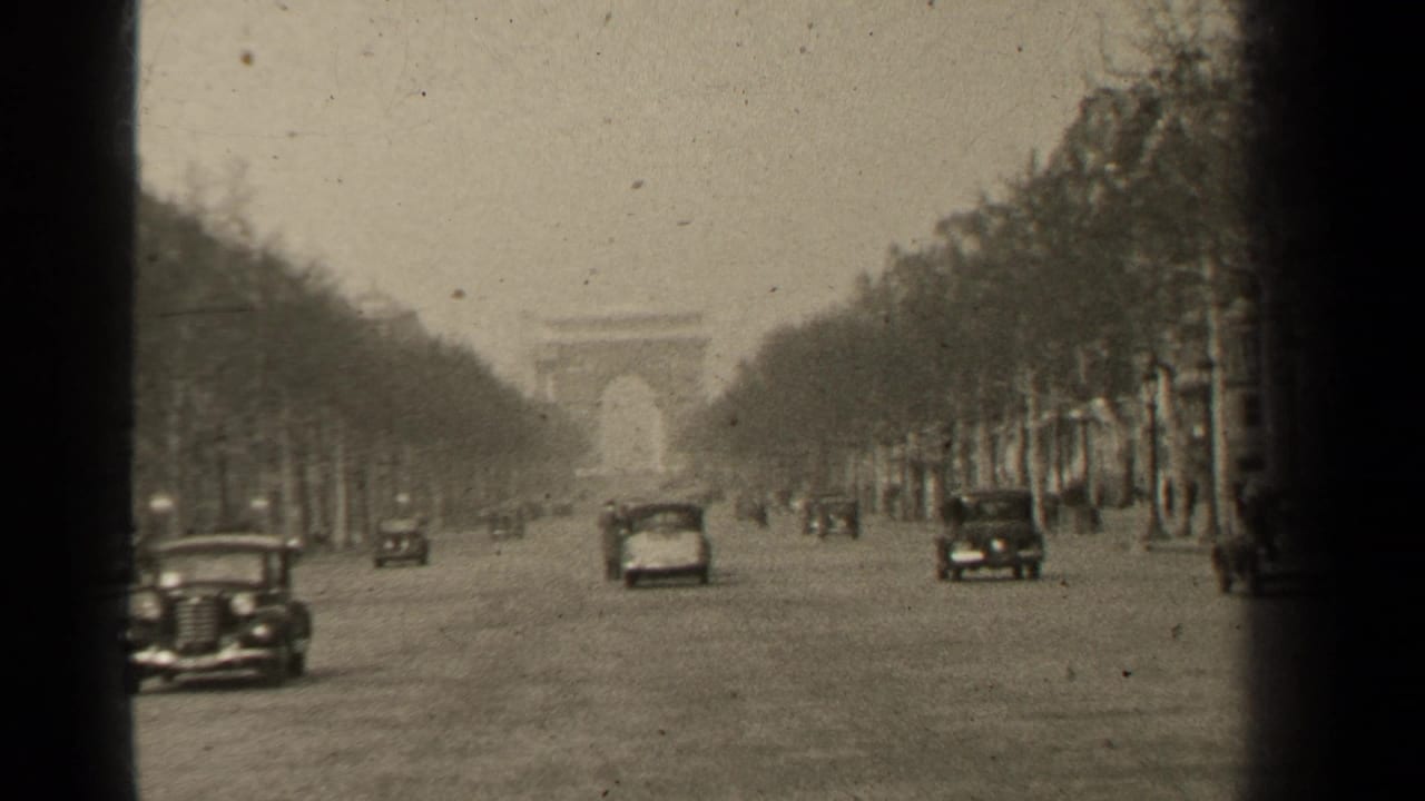 Paris boulevard with old cars, bare trees, and a distant arch-like landmark.