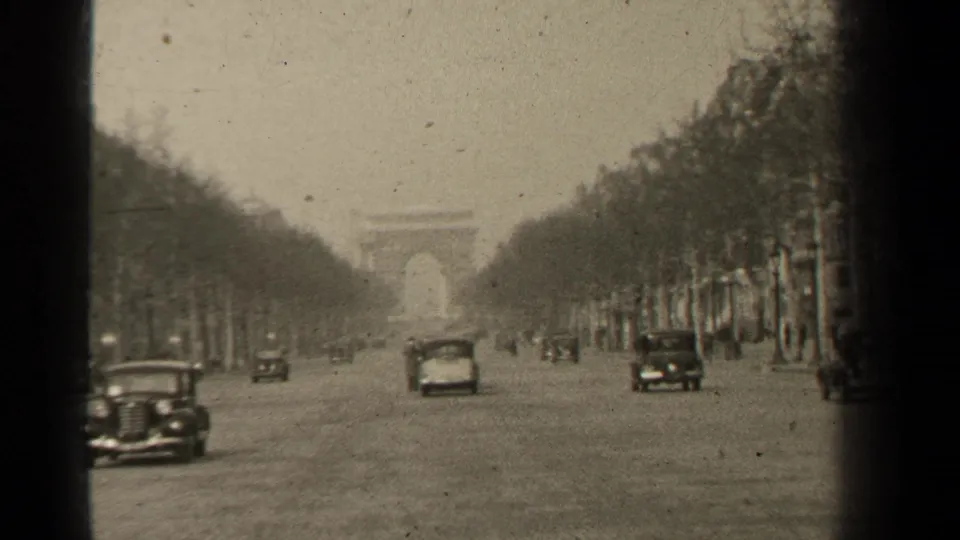 1947 Paris 8mm frame looking down a broad tree-lined avenue with mid-century cars and a distant arch-like landmark.