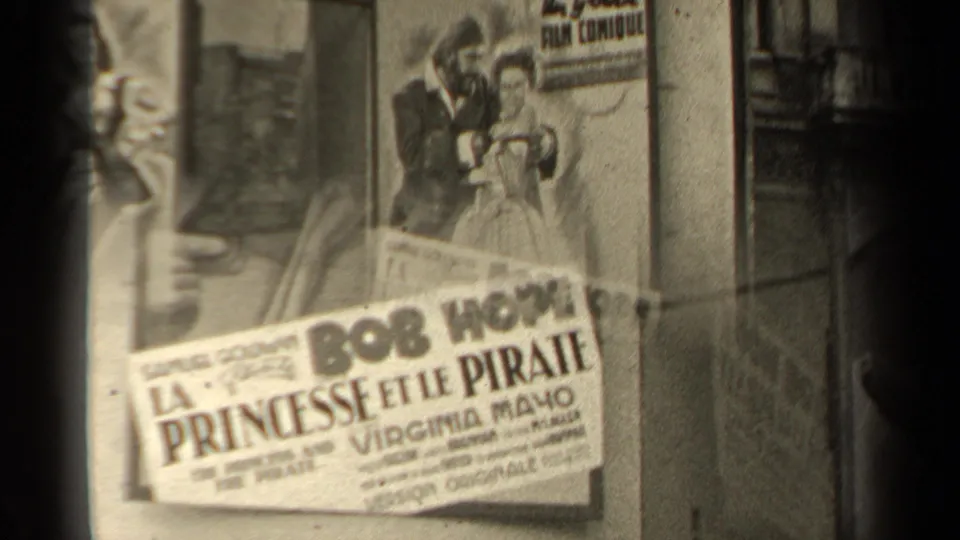 A tilted close-up shows a La Princesse et le Pirate poster with Bob Hope and Virginia Mayo text pasted across other poster artwork on a Paris wall.