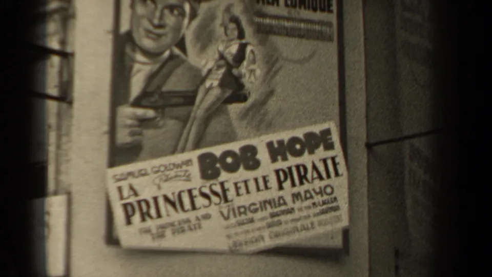 1947 Paris street view showing a French poster for a Bob Hope film, with dark 8mm frame edges and part of a building wall.