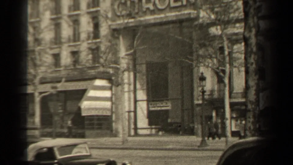 1947 Paris street view with the Citroen sign, small pedestrians near the facade, parked cars, bare trees, and visible home-movie frame shadows.