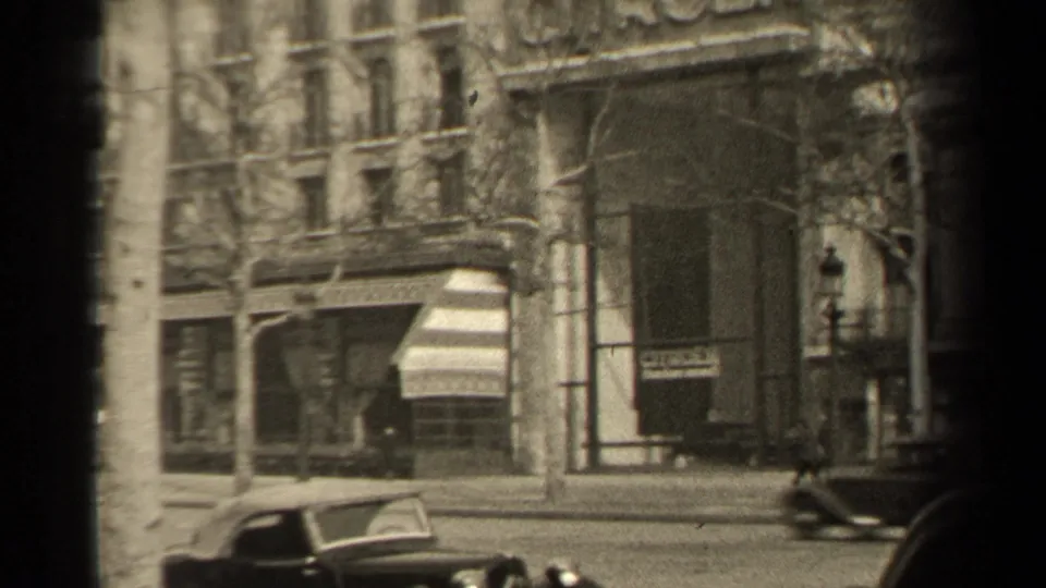 1947 Paris street view with an early automobile passing below bare trees and commercial building facades.