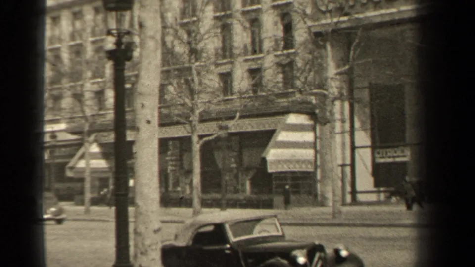 Paris street corner in 1947 with a lamppost, bare trees, commercial windows, and an early automobile.