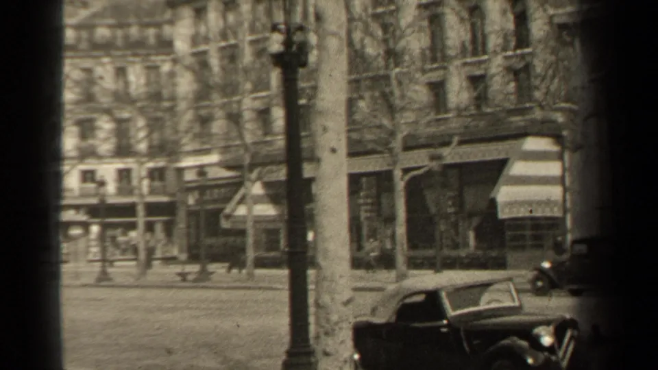 Wide 1947 Paris street frame showing pedestrians, early automobiles, shopfronts, and bare roadside trees.