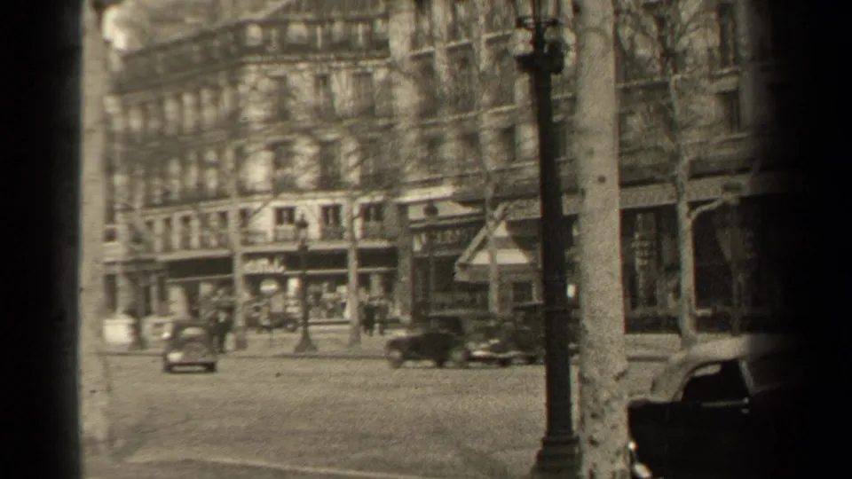 1947 Paris intersection view with early automobiles, distant pedestrians, lampposts, bare trees, and storefronts.