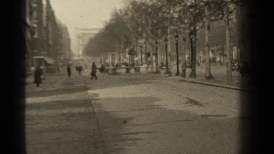 1947 Paris street scene with several pedestrians crossing or walking beside a tree-lined boulevard, with cars, lamps, and buildings in the background.