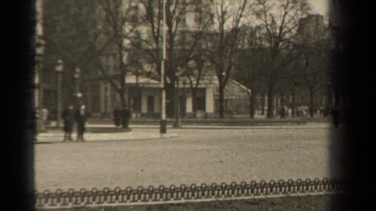 1947 Paris street view with distant pedestrians in dark coats, leafless trees, low decorative fencing, and visible 8mm frame edges.
