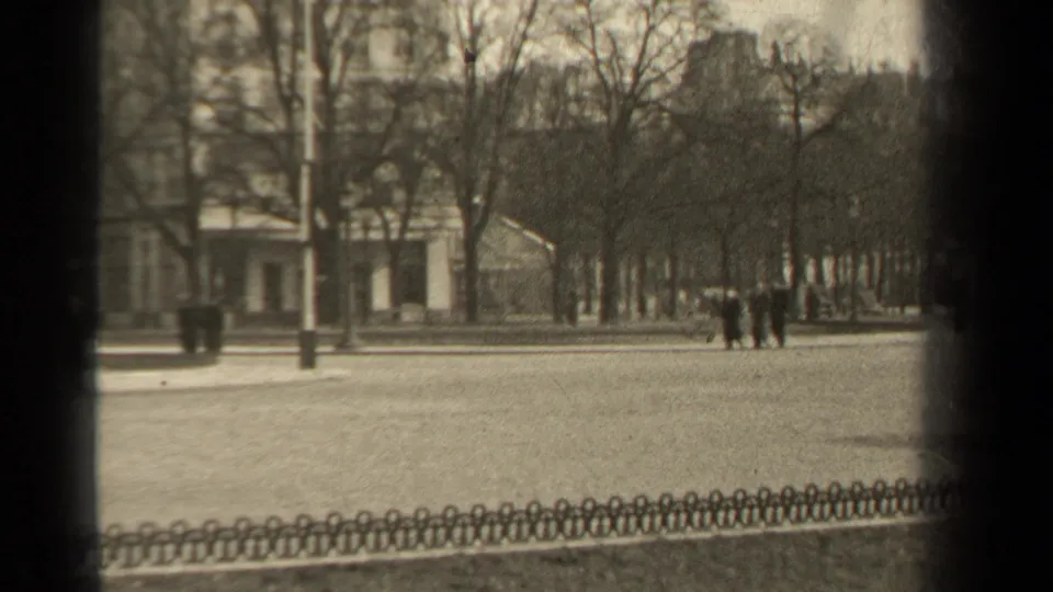 1947 Paris street scene showing a few distant pedestrians, bare tree rows, a tall lamppost, low fencing, and a pale building facade.