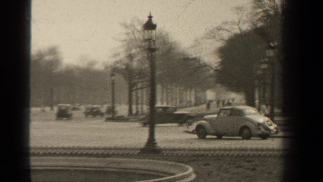 Vintage cars pass a Paris boulevard beside a fountain and lampposts.