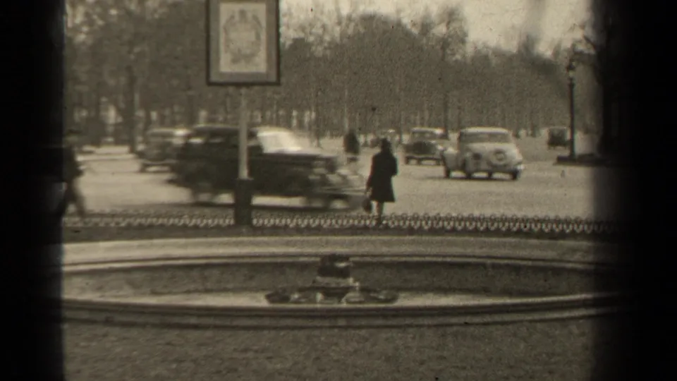 In this 1947 Paris frame, a car blurs across the foreground while pedestrians and other vehicles move beyond a circular fountain.
