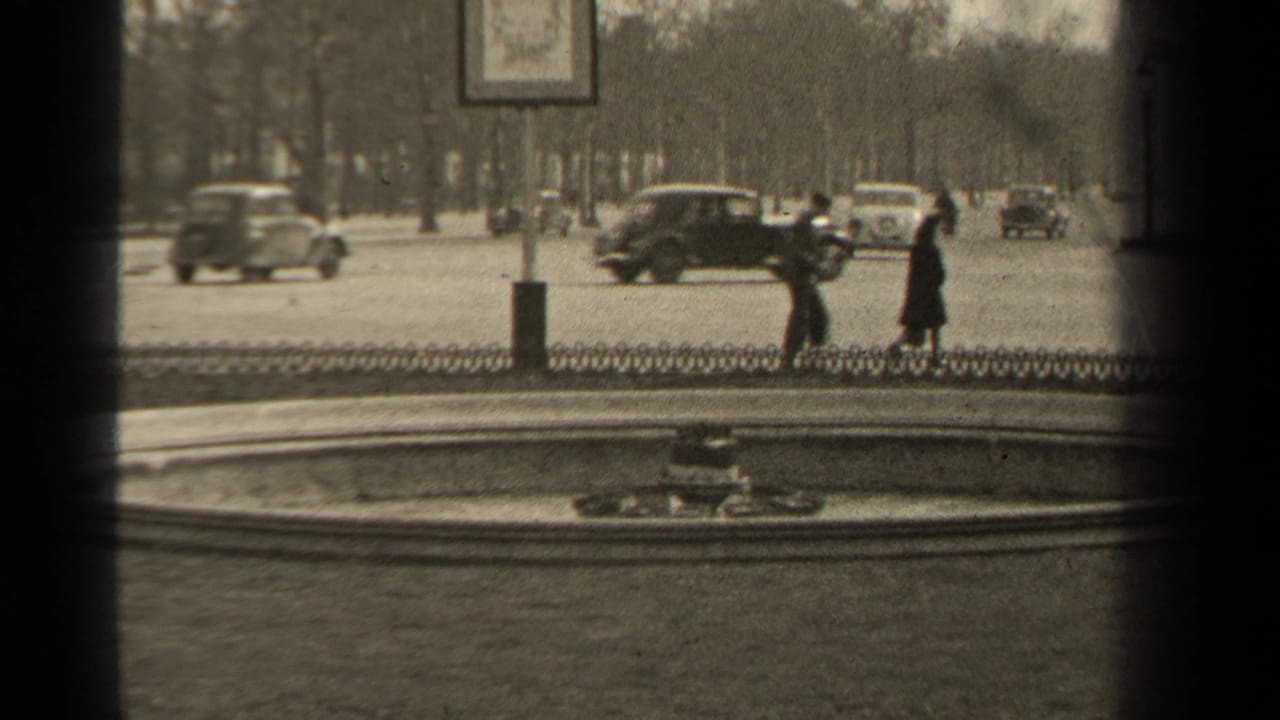 1947 Paris street view with two pedestrians, period cars, bare trees, a low chain fence, and rounded 8mm frame edges.