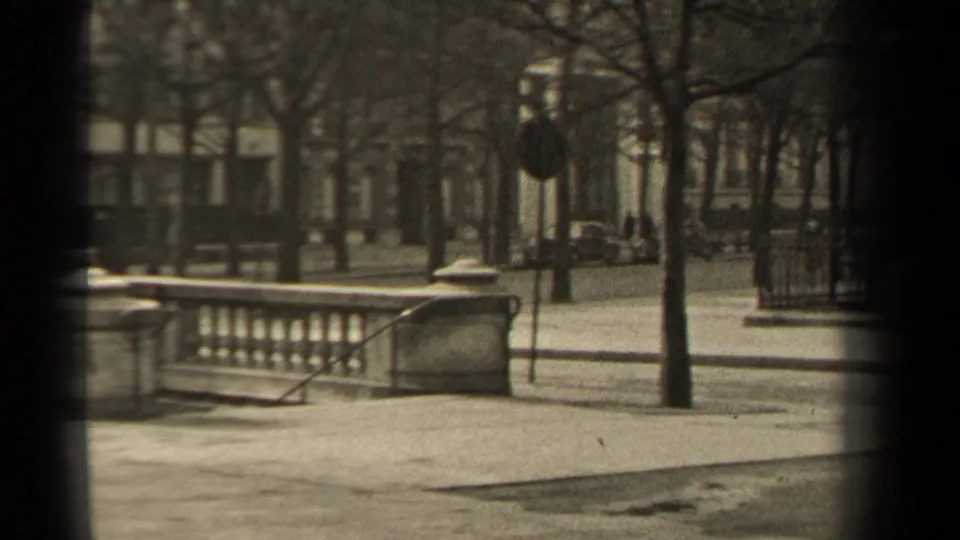 1947 Paris street scene with a stone railing, bare trees, lamppost, sidewalk, and parked cars in the distance.