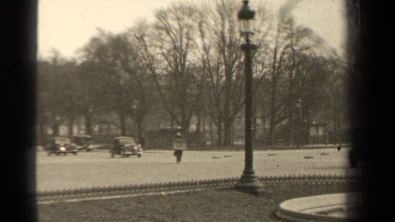 1947 Paris boulevard traffic appears beyond a dark vertical frame, with cars, bare trees, low fencing, and a streetlamp visible.