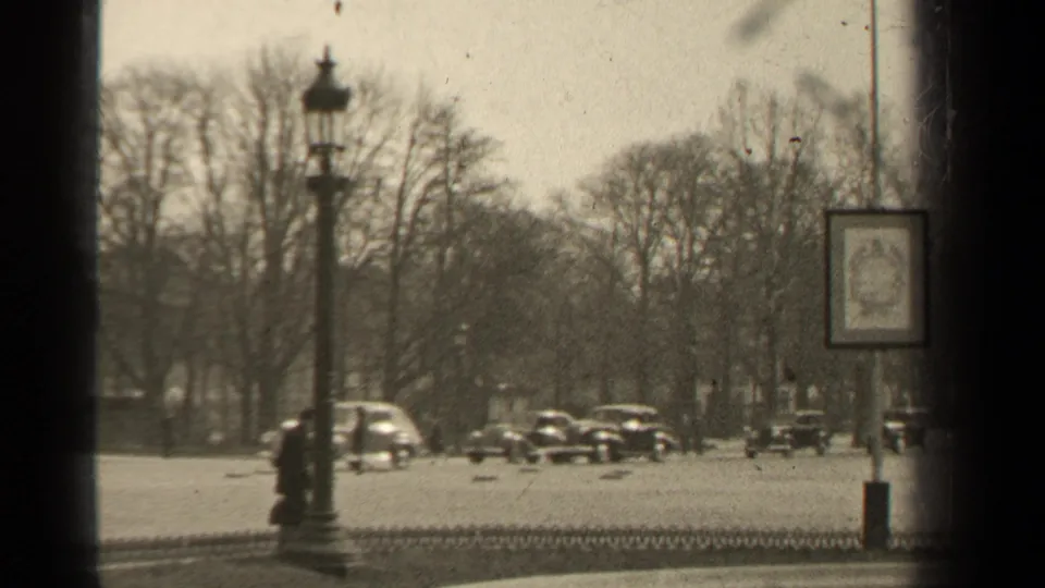 A 1947 Paris boulevard scene shows several cars, pedestrians, bare trees, an iron fence, and a street sign near a lamp post.