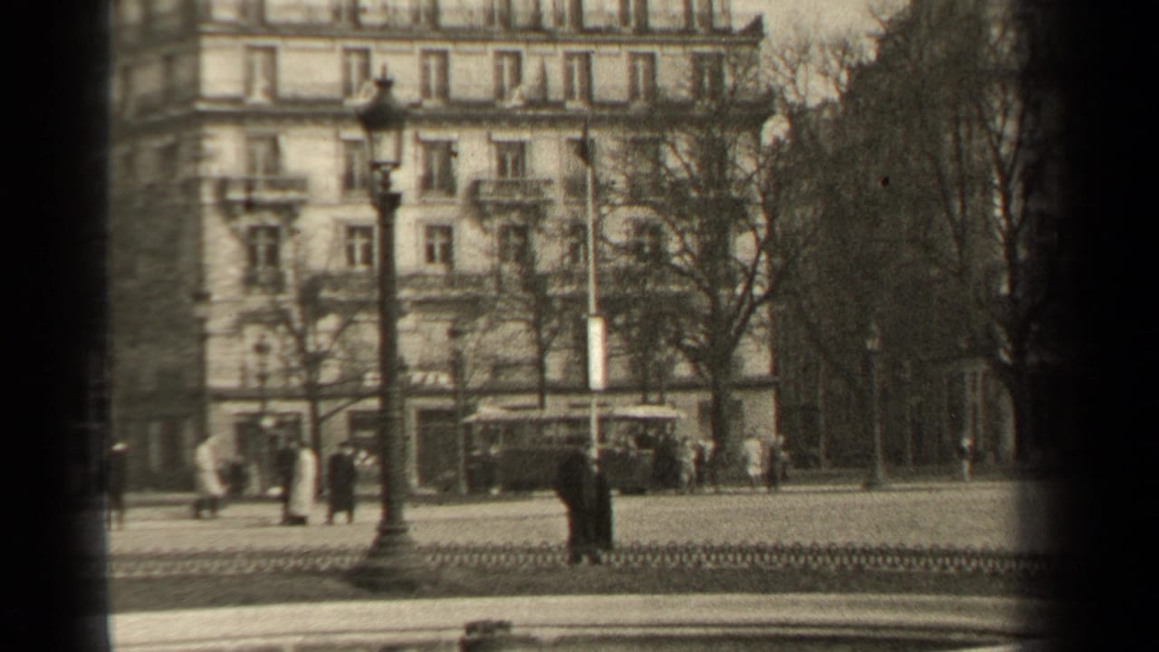 1947 Paris street scene with pedestrians in coats, classic cars, lamps, and a large Haussmann-style facade beside a boulevard.