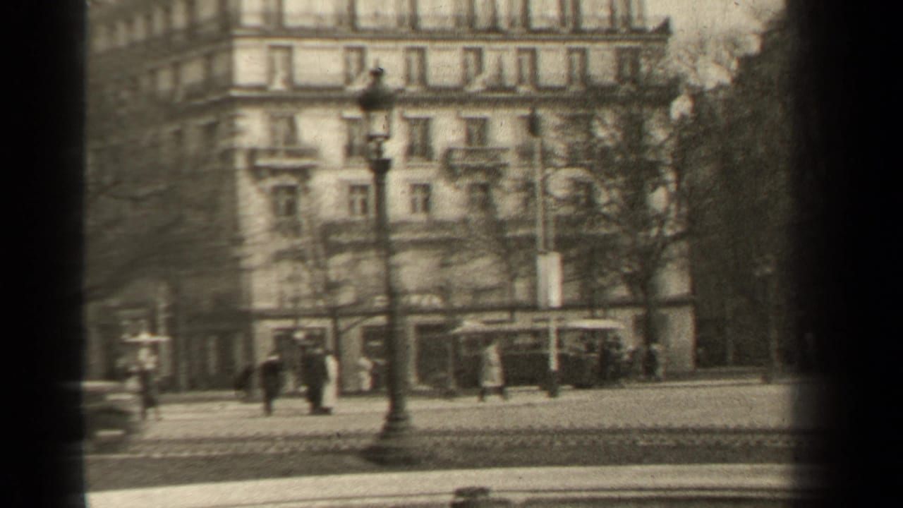 Pedestrians cross or walk near a Paris street with a lamppost and large building behind them.