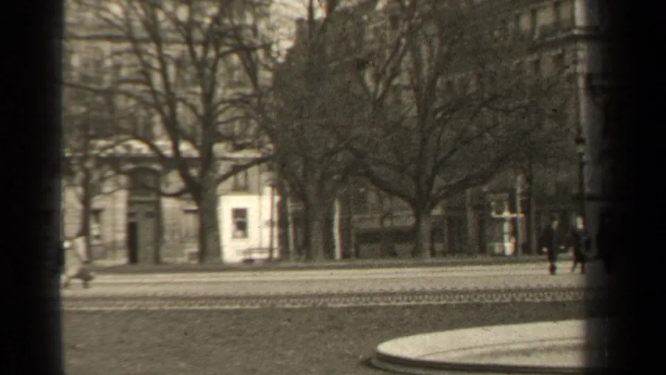 1947 Paris street view with pedestrians near a tree-lined roadway, masonry facades, and dark 8mm frame edges.