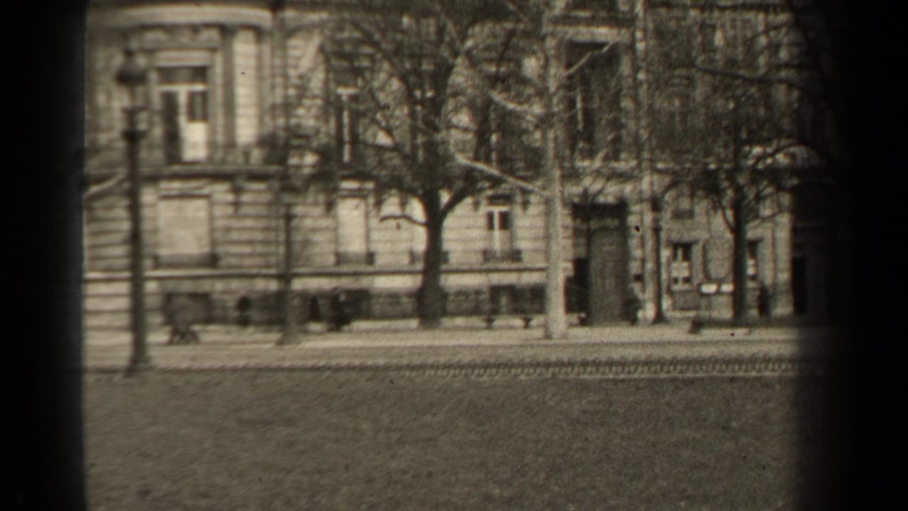 End frame of a 1947 Paris street, showing pedestrians near masonry buildings, bare trees, and tracks across the roadway.