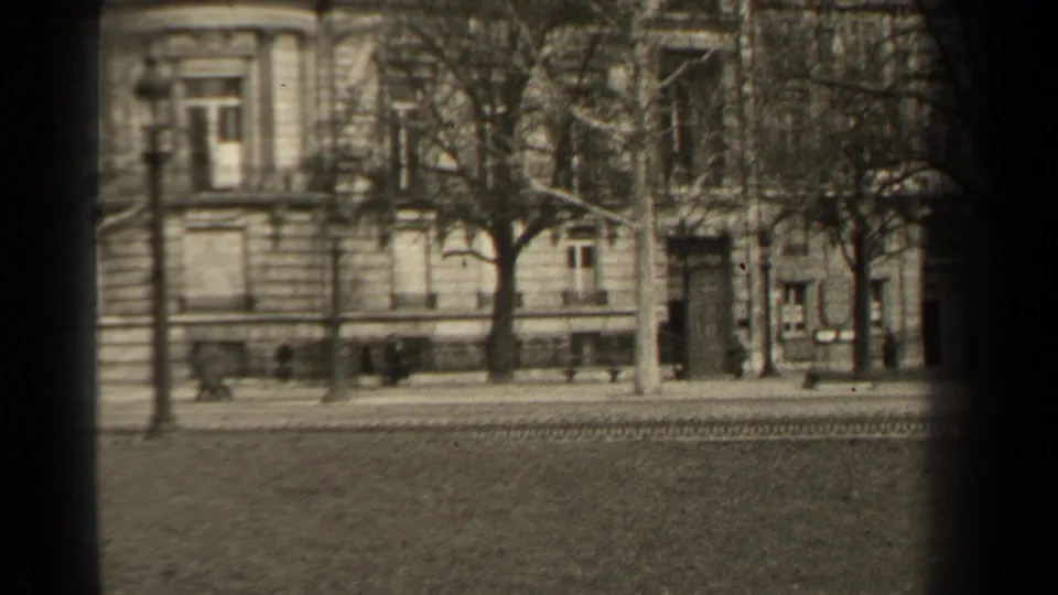 End frame of a 1947 Paris street, showing pedestrians near masonry buildings, bare trees, and tracks across the roadway.