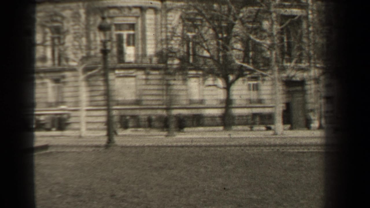 1947 Paris home-movie frame showing a stone facade, bare trees, street lamps, and a quiet boulevard edge.